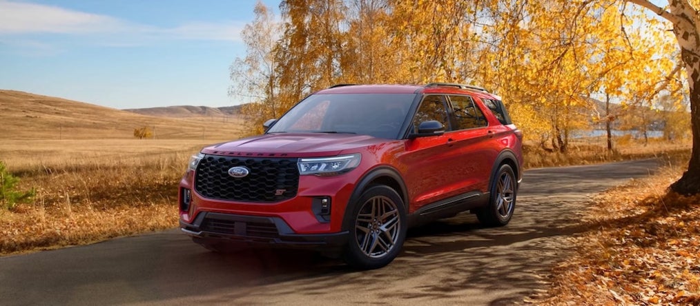 A red 2026 Ford Explorer SUV driving down a country lane in fall