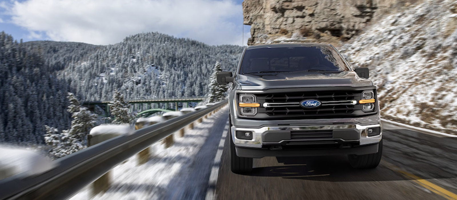 A front view of a dark-colored 2025 Ford F-150 pickup truck driving down a snowy mountain road